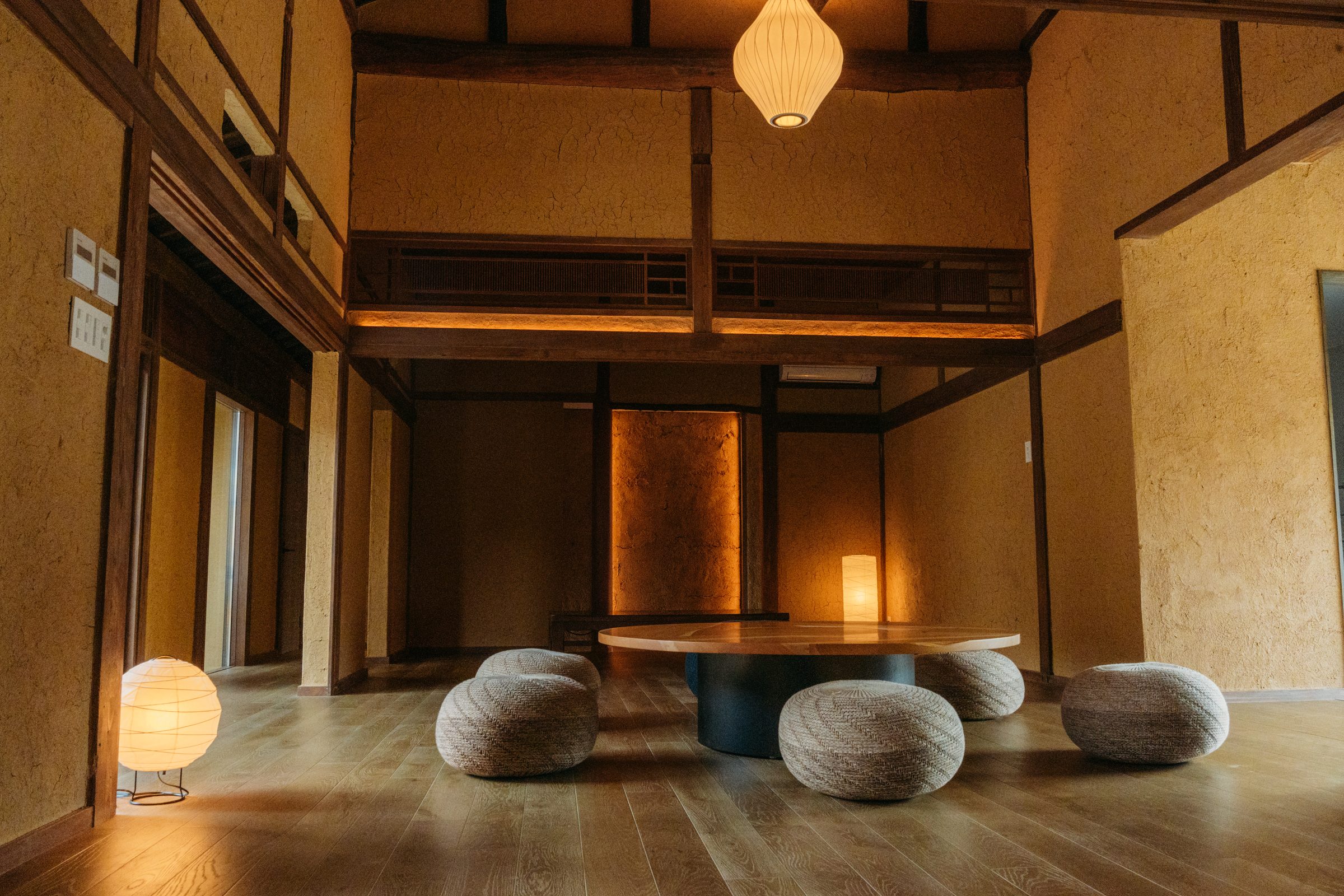 囲炉裏の丸テーブルを囲むリビング。土壁と梁、吹き抜けの明かり